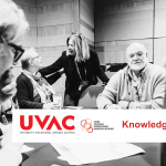 People seated around a table with UVAC associate standing talking to one woman
